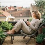 Femme détendue sur balcon urbain avec plantes et thé