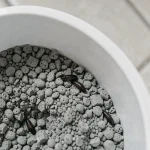 Pupe de mouche visible dans la litière grise d'un bac à chat en plastique blanc, vue de dessus en macro
