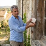 Artisan examinant une fenêtre en bois sur la façade d'une maison en pierre de style provençal pour remplacement de menuiseries