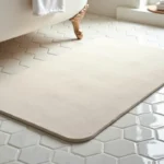 Tapis de bain en diatomite posé sur un carrelage blanc dans une salle de bain épurée, texture poreuse apparente